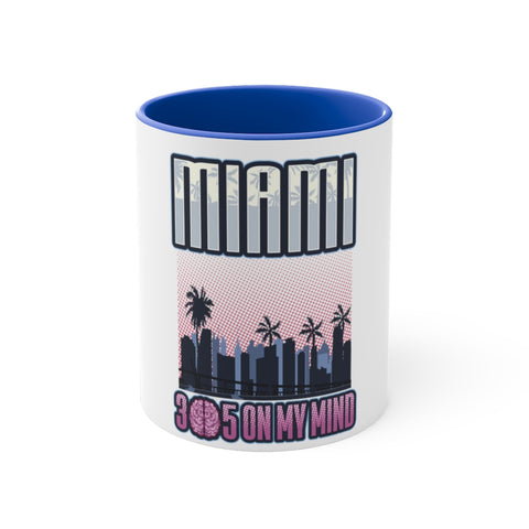 A white ceramic mug with blue accents and a design that includes the text 'Miami' and a graphic of a city skyline at dusk.